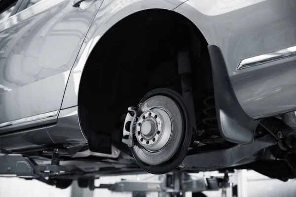 Modern car on hydraulic lift at automobile repair shop, closeup