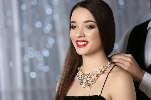 Hombre poniendo joyas en hermosa mujer joven contra las luces borrosas, espacio para el texto — Foto de Stock