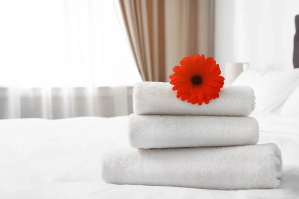 Pilha de toalhas frescas com flor na cama dentro de casa. Espaço para texto — Fotografia de Stock