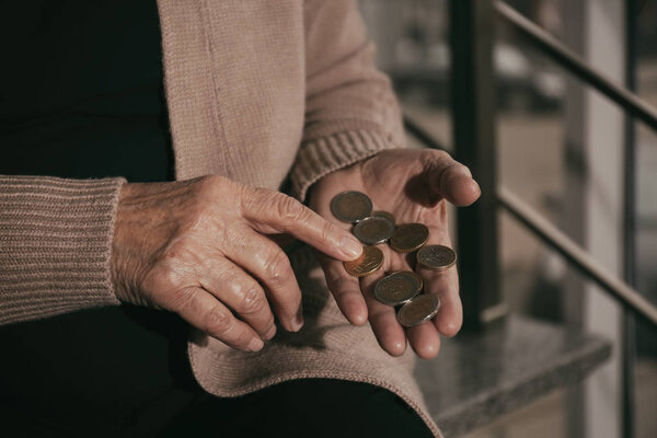 Poor senior woman with coins on stairs, closeup