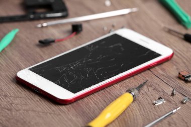Masaüzerinde kırık ekran ve onarım araçları ile modern telefon