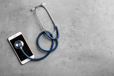 Kırık ekranlı modern akıllı telefon, stetoskop ve masadaki metin alanı, düz yatıyordu. Cihaz onarım hizmeti