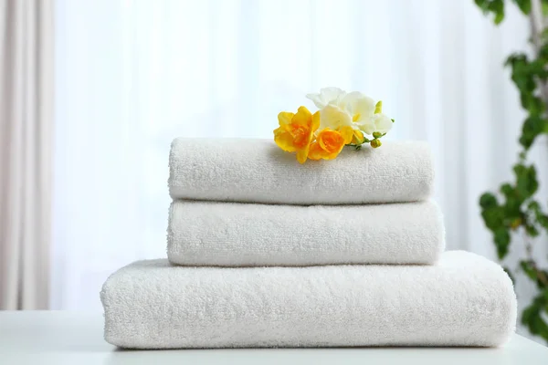 Stack of fresh towels with flowers on table indoors — Stock Photo, Image