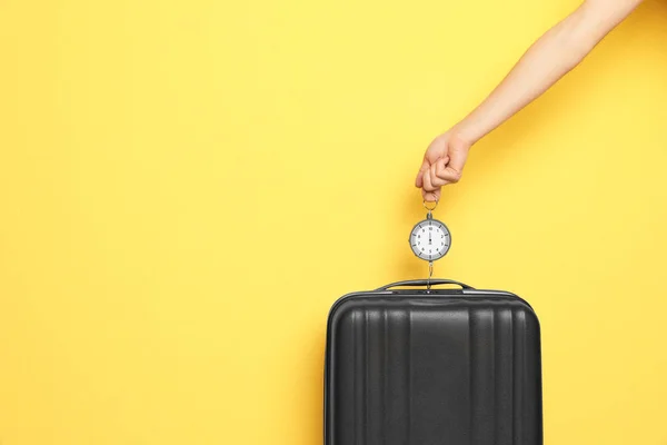 Woman weighing suitcase against color background, closeup. Space for text