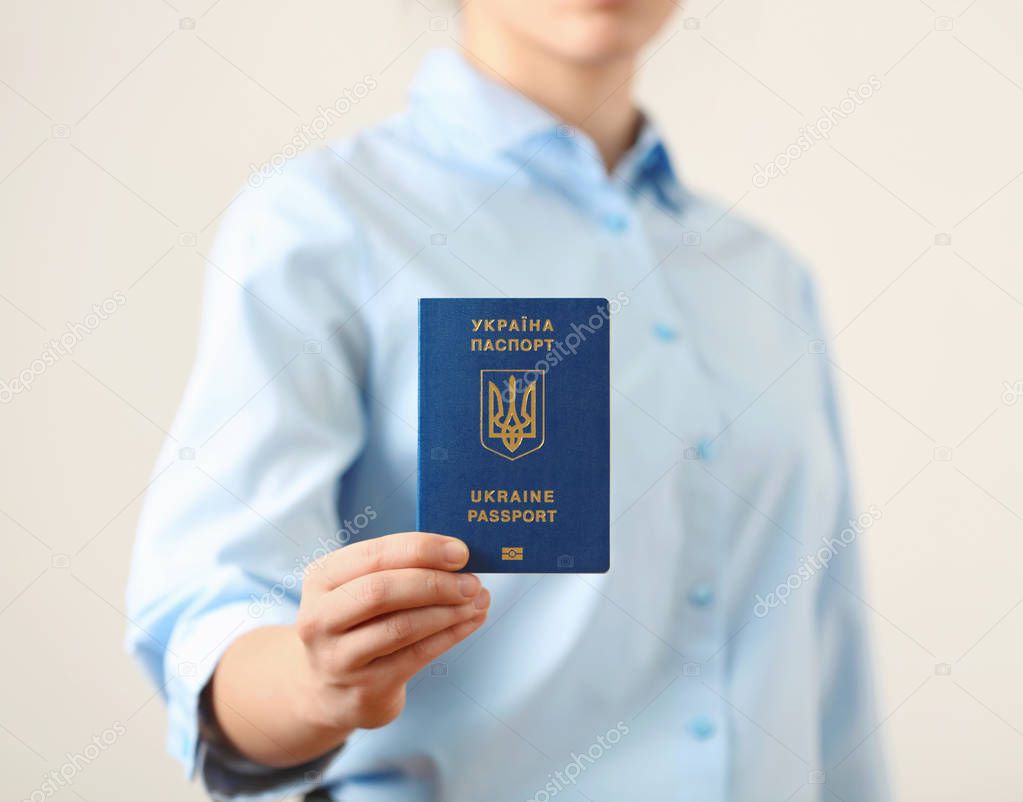 Woman holding Ukrainian travel passport on light background, closeup. International relationships