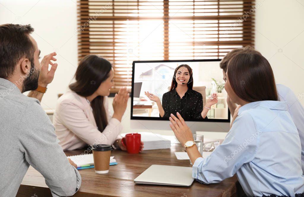 People having video chat with colleague at table in office