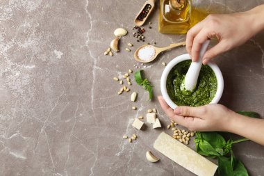 Kadın pesto sosunu gri masada havan topuzuyla karıştırıyor. Metin için boşluk