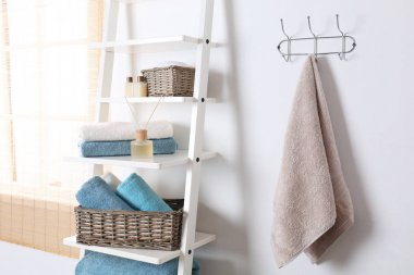Beyaz duvara yakın temiz havlu ve banyo malzemeleri ile raf ünitesi ve raf