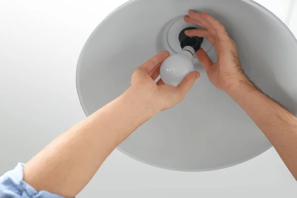 Man changing light bulb in lamp indoors, closeup