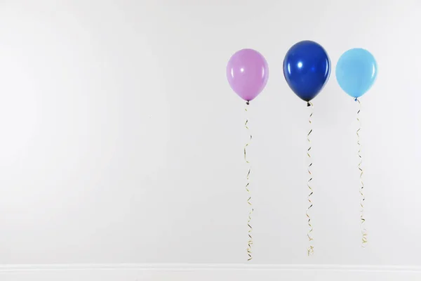 Diferentes balões brilhantes contra a parede de luz, espaço para texto. Tempo de celebração — Fotografia de Stock