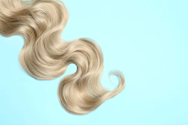 Serrure de cheveux blonds ondulés sur fond de couleur, vue de dessus. Espace pour le texte — Photo