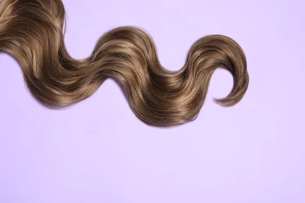 Serrure de cheveux bruns ondulés sur fond de couleur, vue de dessus. Espace pour le texte — Photo