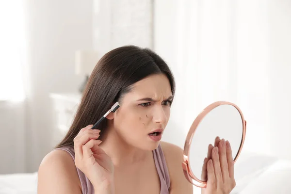 Mooie vrouw met gevallen wimpers en cosmetische borstel op zoek naar spiegel binnenshuis — Stockfoto