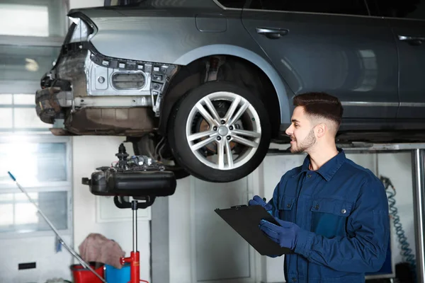 Tekniker som kontrollerar bil på hydraulisk lyft i bilverkstad — Stockfoto