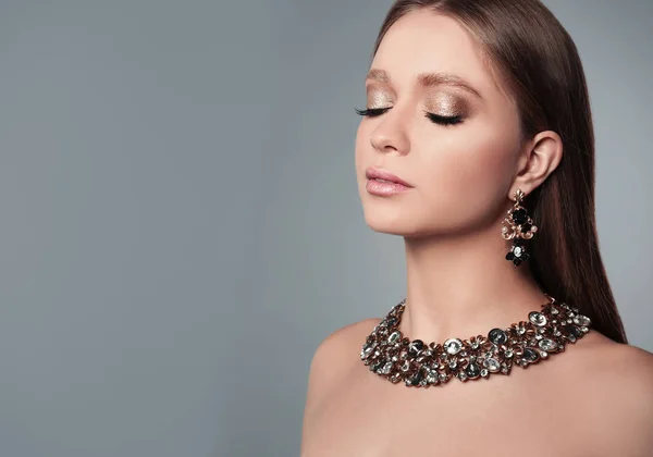 Hermosa mujer con joyas elegantes sobre fondo gris, espacio para el texto — Foto de Stock