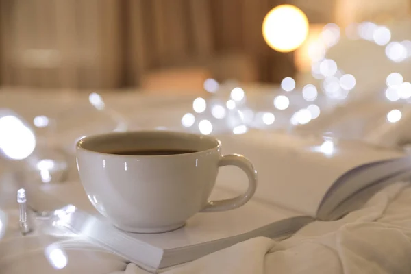 Kopje koffie en boek op bed tegen onscherpe achtergrond. Ruimte voor tekst — Stockfoto