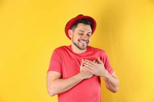 Portrait of handsome man holding hands near his heart on color background — Stock Photo, Image