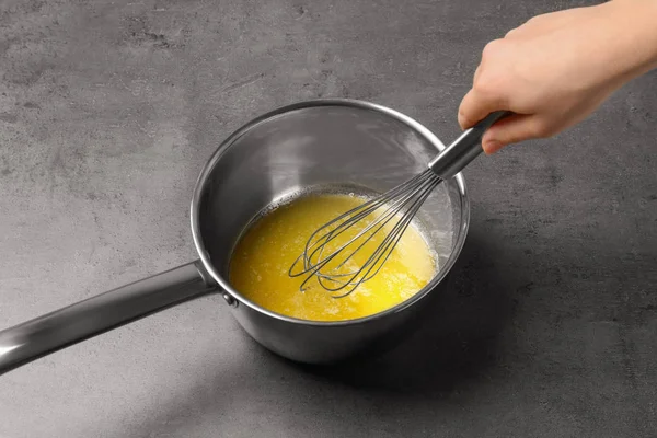 Femme fouettant le beurre fondu dans une casserole sur une table grise, gros plan — Photo