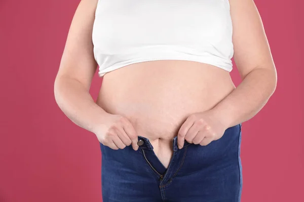 Mujer con sobrepeso tratando de usar jeans ajustados en el fondo de color, primer plano — Foto de Stock