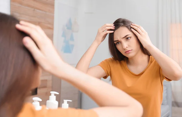 Молодая женщина с проблемой выпадения волос смотрит в зеркало в помещении — стоковое фото