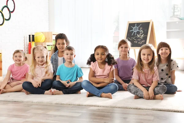 Groep van schattige kleine kinderen zittend op de vloer binnenshuis. Kleuterschool speeltijd activiteiten — Stockfoto