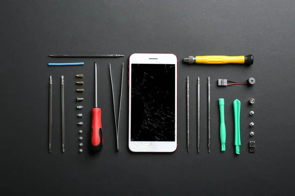 Flat lay composition with broken mobile phone and repair tools on color background