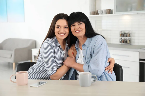 Portrait of young woman and her mature mother at table indoors — Stock Photo, Image