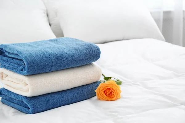 Stack of clean towels and beautiful rose flower on bed. Space for text — Stock Photo, Image