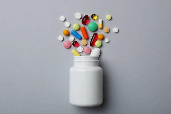 Bottiglia con diverse pillole su sfondo grigio, posa piatta — Foto Stock