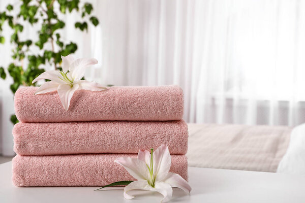 Stack of fresh towels with flowers on table in bedroom. Space for text