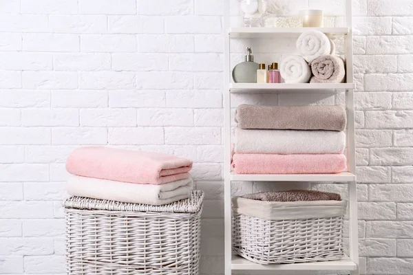 Unidade de prateleira e cestas com toalhas limpas e produtos de higiene pessoal perto da parede de tijolo — Fotografia de Stock