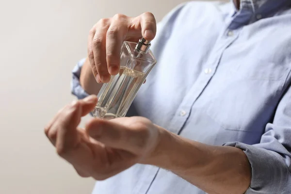 Man aanbrengen van parfum op pols tegen lichte achtergrond, close-up — Stockfoto
