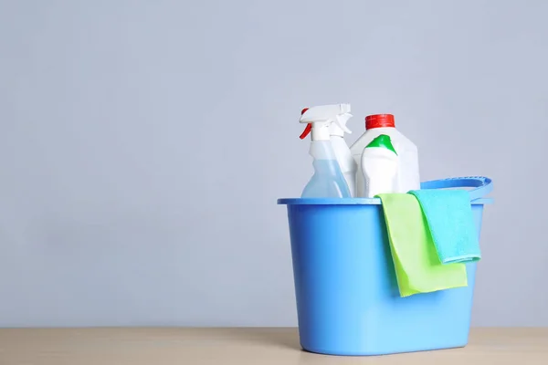 Cubo con artículos de limpieza sobre la mesa sobre fondo gris. Espacio para texto — Foto de Stock