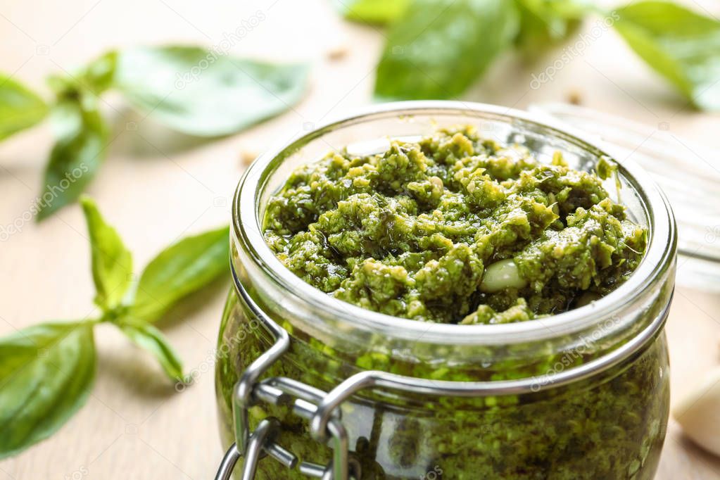 Jar of tasty pesto sauce on table, closeup. Space for text