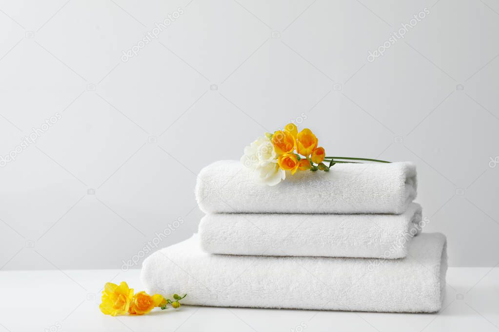 Stack of fresh towels with flowers on table against white background. Space for text