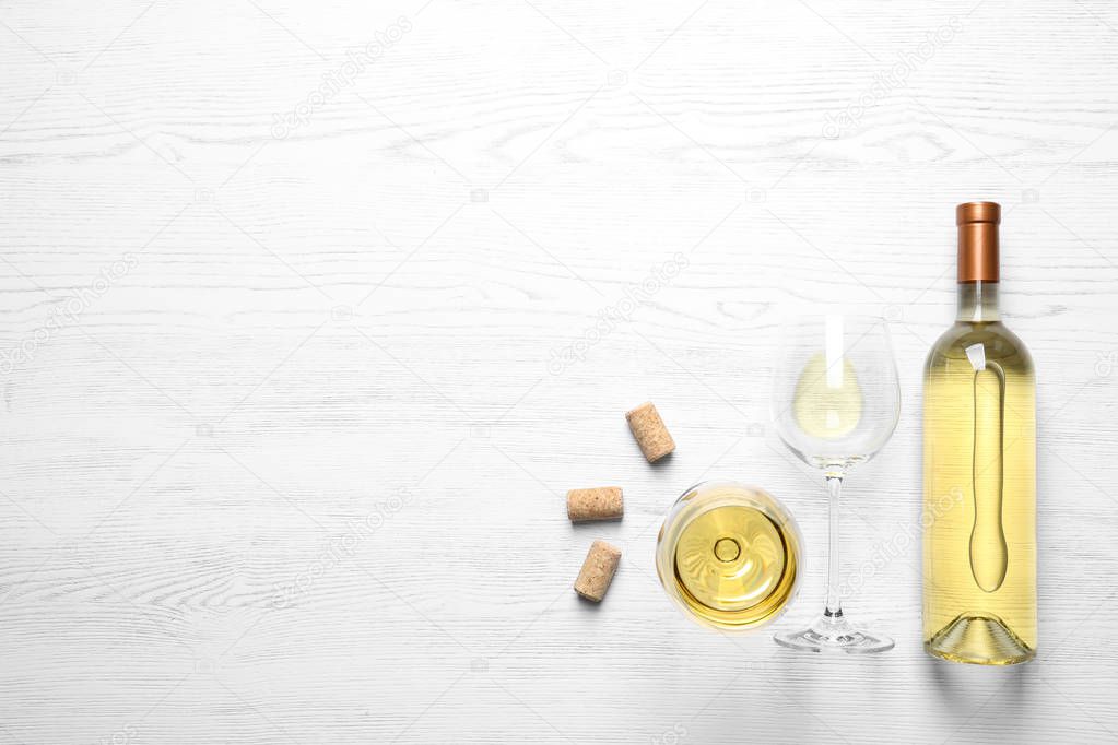 Glasses and bottle with white wine on wooden background, flat lay. Space for text