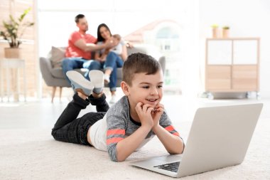 Evde ailesinin yanında halı üzerinde yatan dizüstü bilgisayar ile çocuk
