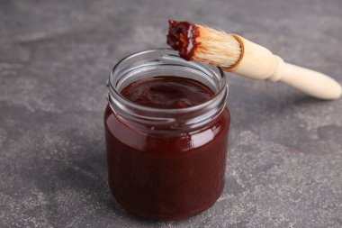 Gri arka planda barbekü soslu kavanoz ve fırça