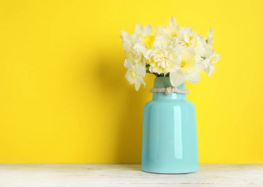 Renkli arka plana karşı masada vazoda nergis buketi, metin için alan. Taze bahar çiçekleri