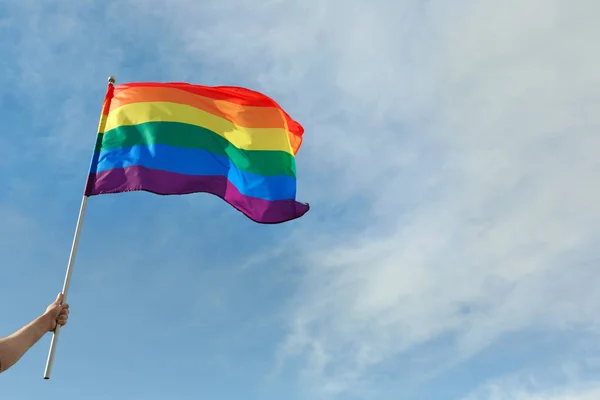 Hombre gay sosteniendo bandera LGBT arco iris contra el cielo azul. Espacio para texto — Foto de Stock