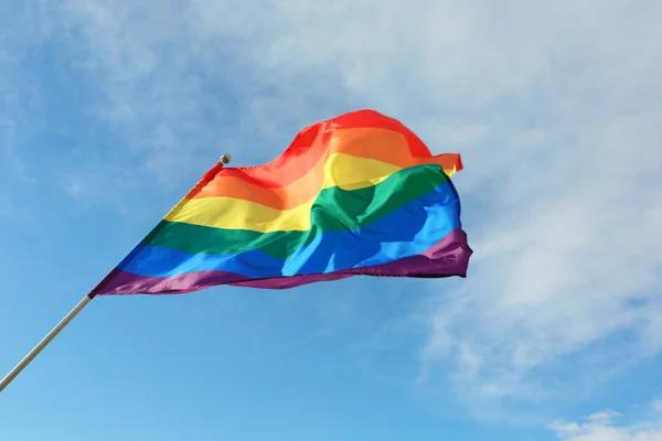 Arco-íris brilhante bandeira gay balançando contra o céu azul. Comunidade LGBT — Fotografia de Stock