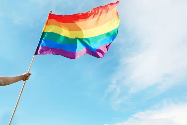 Gay man holding rainbow LGBT flag against blue sky. Space for text — Stock Photo, Image
