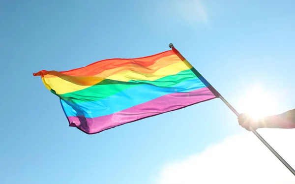 Gay hombre la celebración de arco iris LGBT bandera contra azul cielo — Foto de Stock