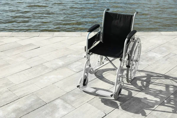 Lege rolstoel in de buurt van de rivier op zonnige dag. Ruimte voor tekst — Stockfoto