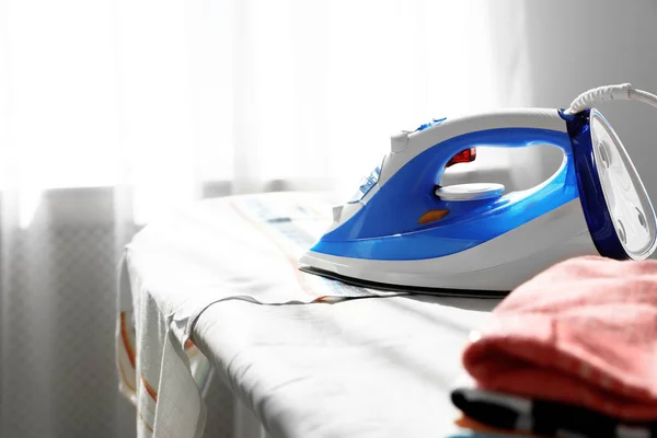 Modern electric iron on board indoors, space for text. Household appliance — Stock Photo, Image