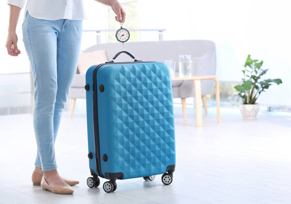 Женщина взвешивает чемодан в помещении. Пространство для текста
