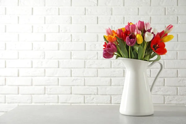 Ваза з красивими весняними квітами тюльпанів на столі біля цегляної стіни. Простір для тексту — стокове фото