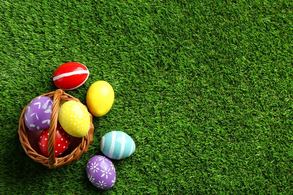 Cesto di vimini con uova di Pasqua dipinte su erba verde, vista dall'alto. Spazio per testo — Foto Stock
