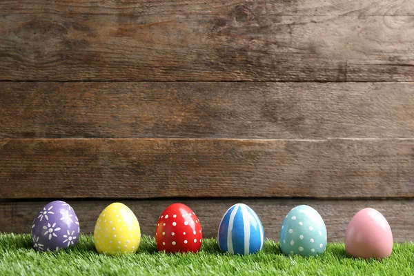 Ahşap arka plan, metin için alan karşı yeşil çim üzerinde Boyalı Paskalya yumurtaları — Stok fotoğraf