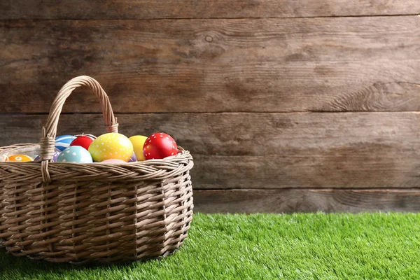 Cesta de mimbre con huevos de Pascua pintados sobre hierba verde sobre fondo de madera, espacio para texto —  Fotos de Stock